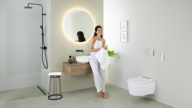 Ženska osoba se naslanja na umivaonik u kupatilu s Geberit AquaClean Sela WC šoljom sa tušem i Geberit VariForm umivaonikom i nameštajem