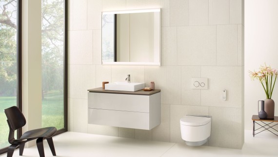 Belo kupatilo sa elementom sa ogledalom, ormarićem, tipkom za aktiviranje ispiranja i keramičkim elementima kompanije Geberit